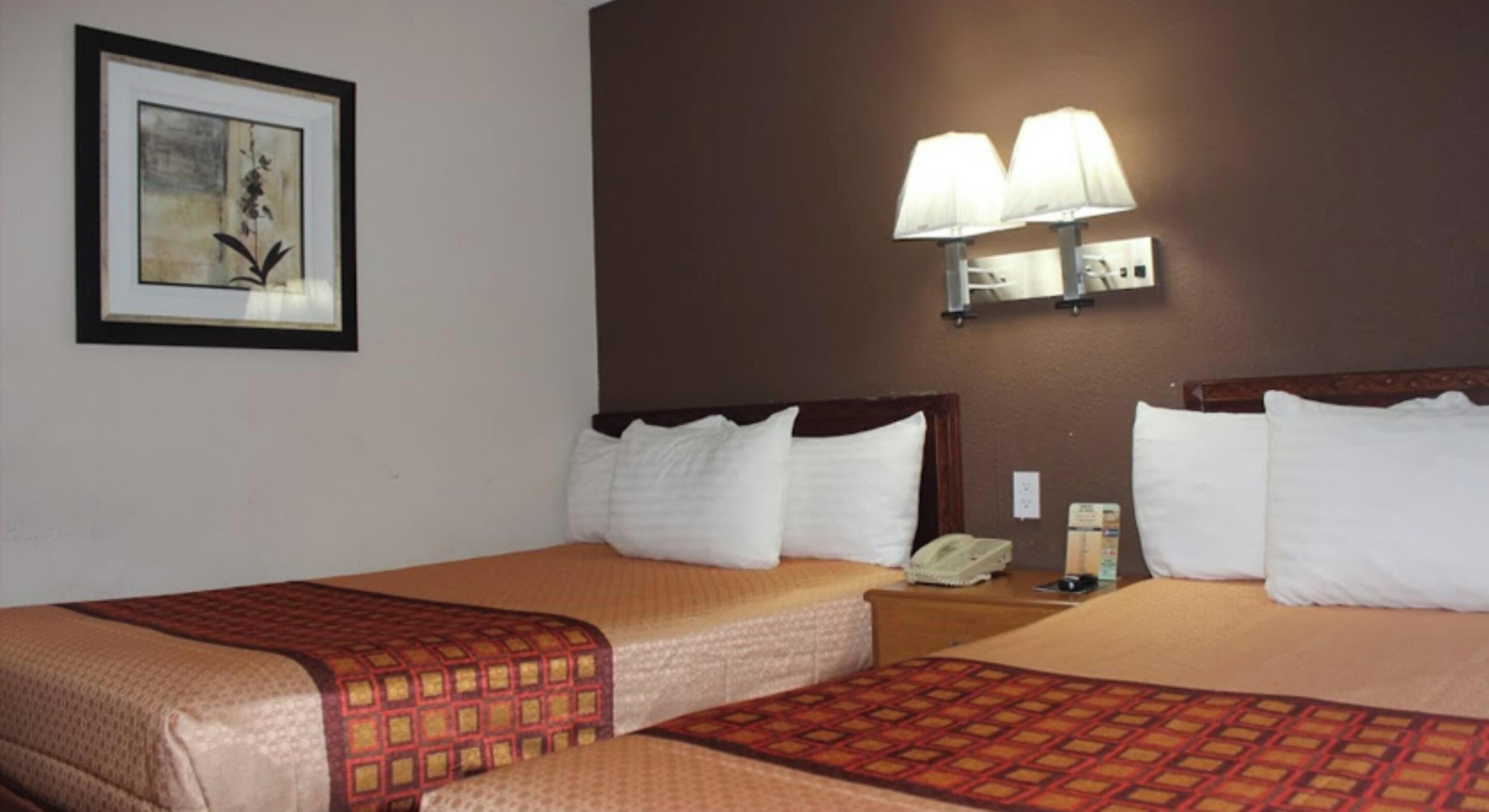 Een hotelkamer met twee bedden, een ingelijste afbeelding aan de muur en een wandlamp.