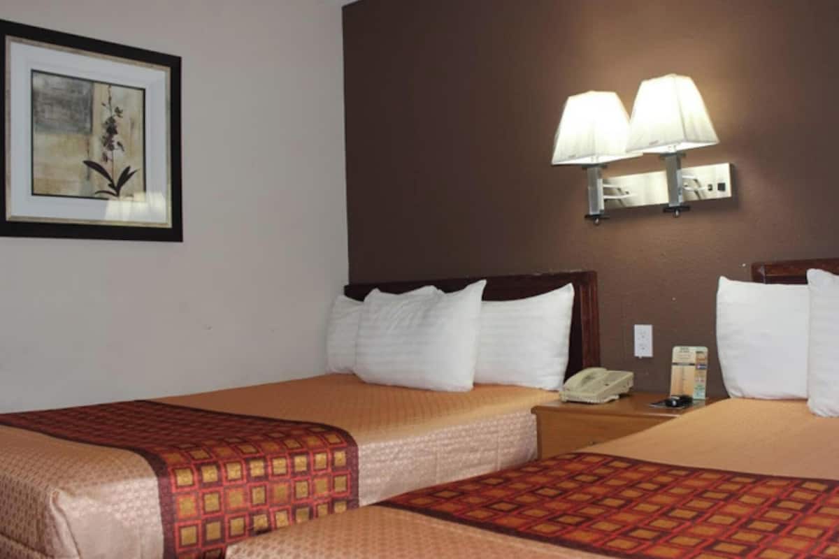 Habitación de hotel con dos camas, una obra de arte enmarcada en la pared y una lámpara fijada a la pared.
