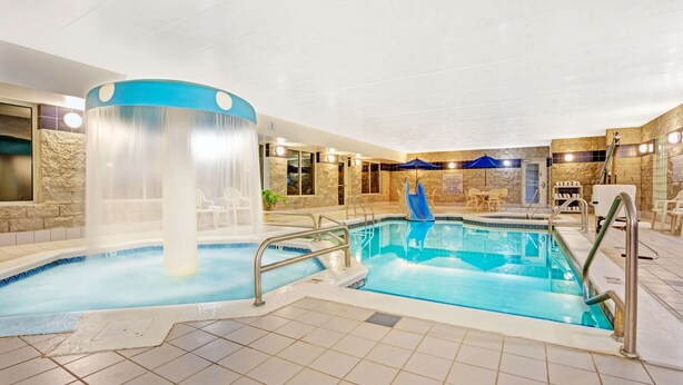 Une piscine intérieure dotée d’un jacuzzi, d’un revêtement de sol carrelé et d’un espace détente avec des fauteuils.