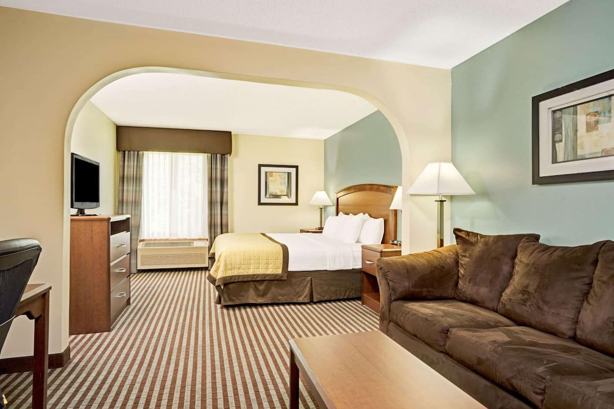 Une chambre d’hôtel équipée d’un lit, d’un bureau, d’une télévision, d’un canapé et d’une grande fenêtre avec des rideaux.