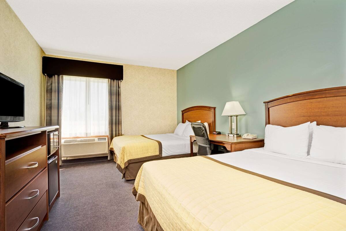 Une chambre d’hôtel avec deux lits, un bureau, une chaise, une télévision et une lampe.