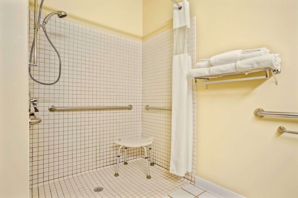 Un baño con ducha, barras de apoyo, un perchero blanco y un taburete pequeño blanco.