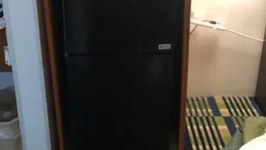 Een compacte koelkast en magnetron in een hoek van een kamer met een gestreepte vloer.