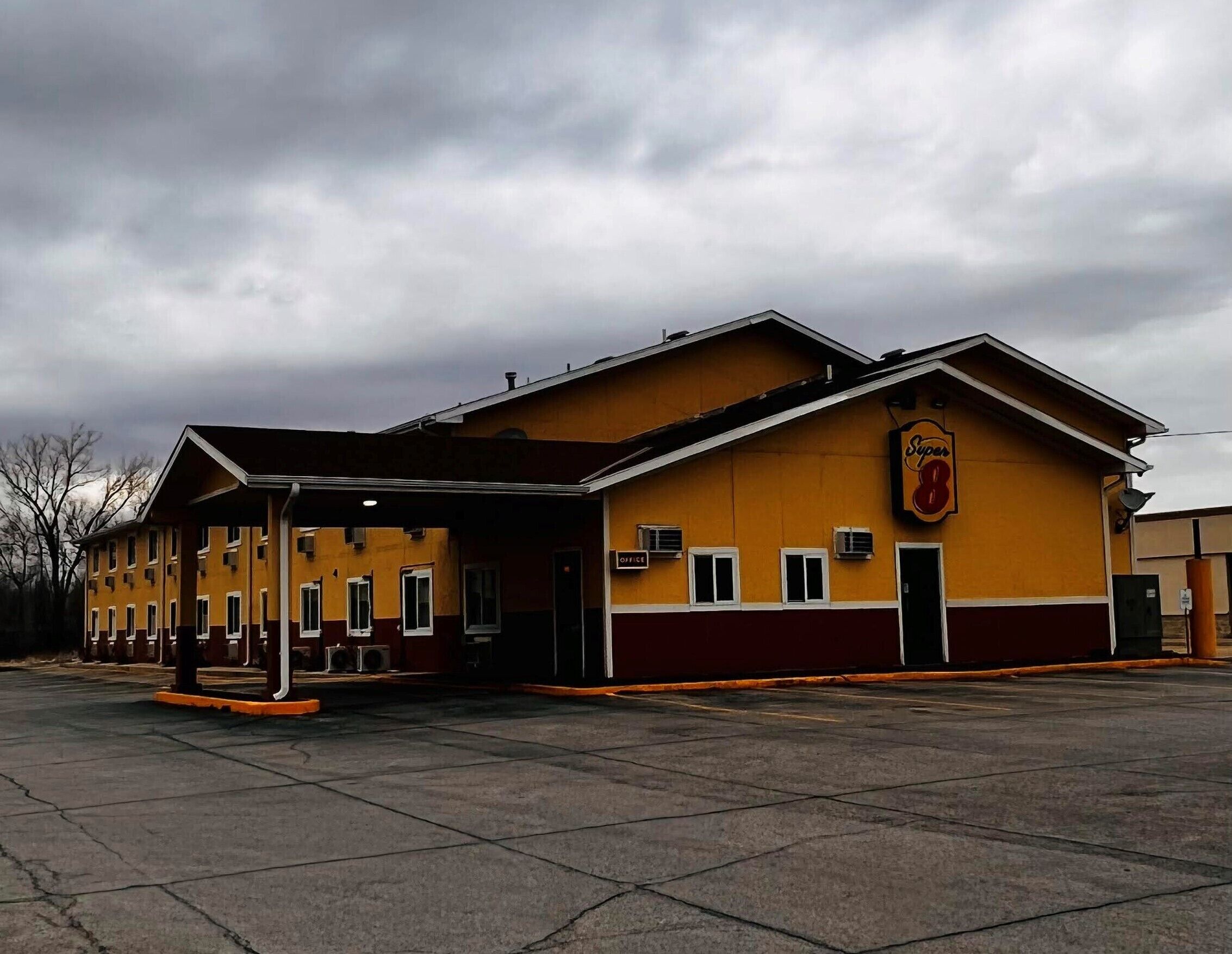 Un edificio amarillo con un letrero Super 8, un acceso cubierto y un estacionamiento.