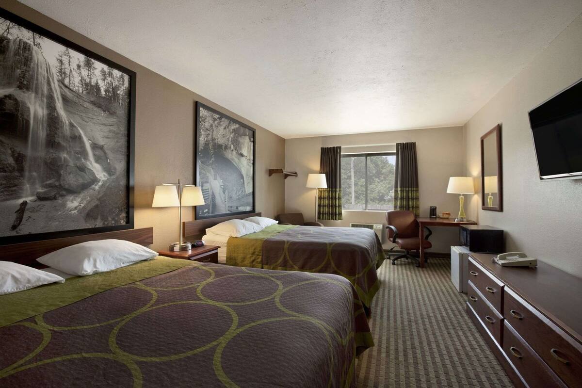 A hotel room with two beds, a desk, a chair, a TV, and a window with curtains.