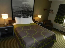 A hotel room with a large bed, two bedside tables with lamps, a chair, a coat rack, and a large framed picture on the wall.