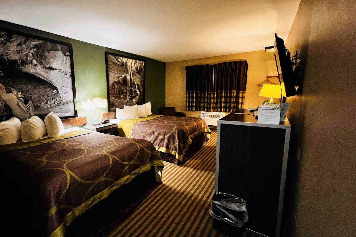 A hotel room with two beds, a desk, a lamp, and artwork on the walls.