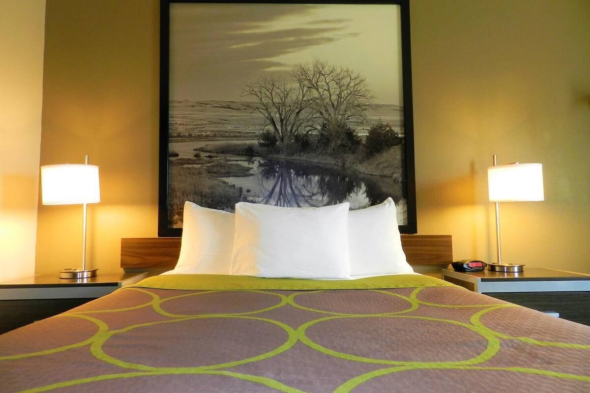 A hotel room with a large bed, two bedside lamps, a framed landscape painting, and a patterned bedspread.
