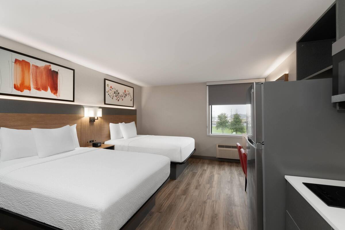 Ein Hotelzimmer mit zwei Betten, einem Kühlschrank, einem Fenster mit Blick und Bildern an den Wänden.
