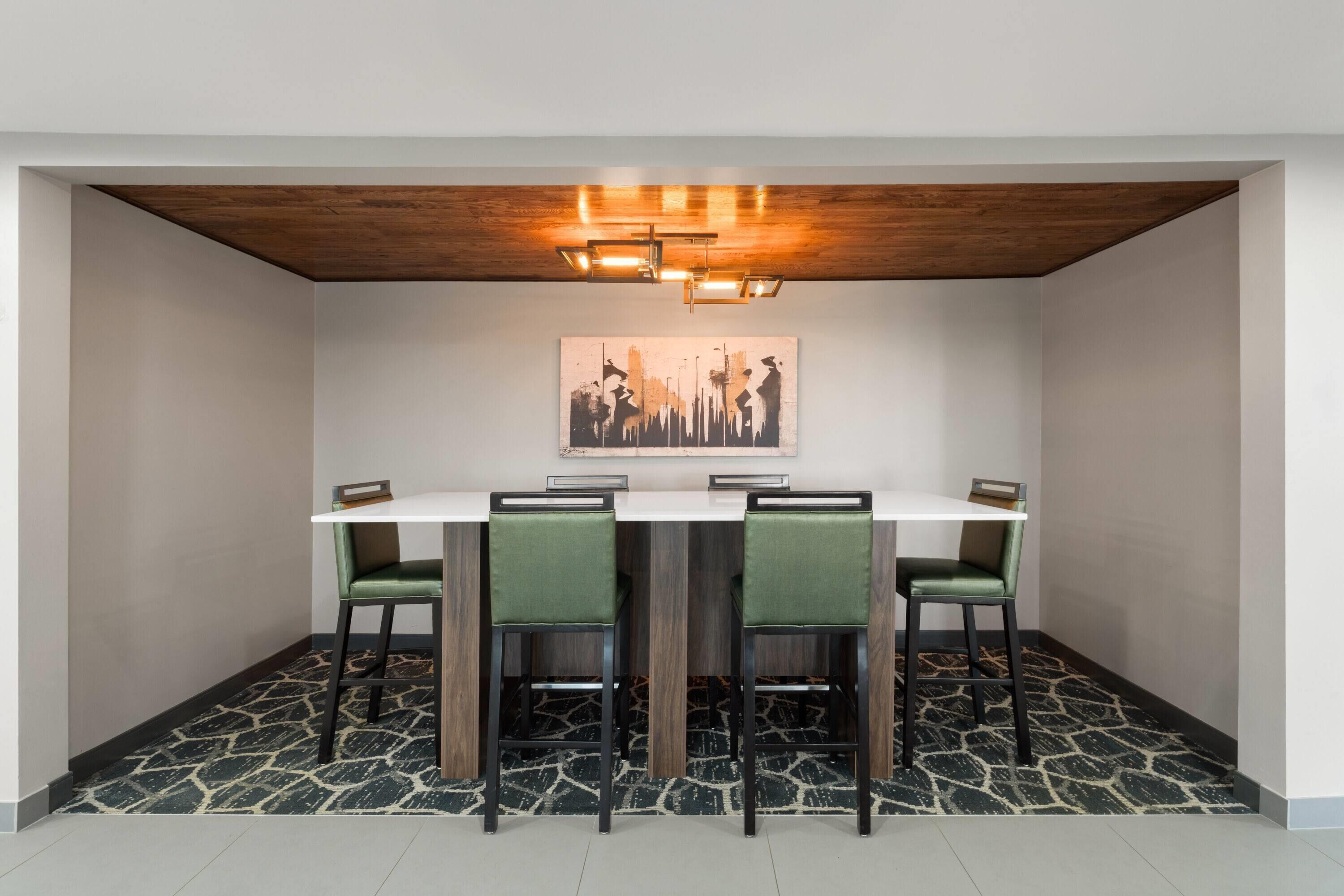 A dining area with a white table, four green chairs, a cityscape artwork on the wall, and a patterned floor.
