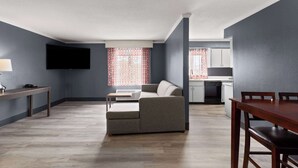 A modern living room with a grey sofa, wooden dining table, and a flat-screen TV mounted on the wall. - La Quinta Inn & Suites by Wyndham Goodlettsville - Nashville (Goodlettsville)