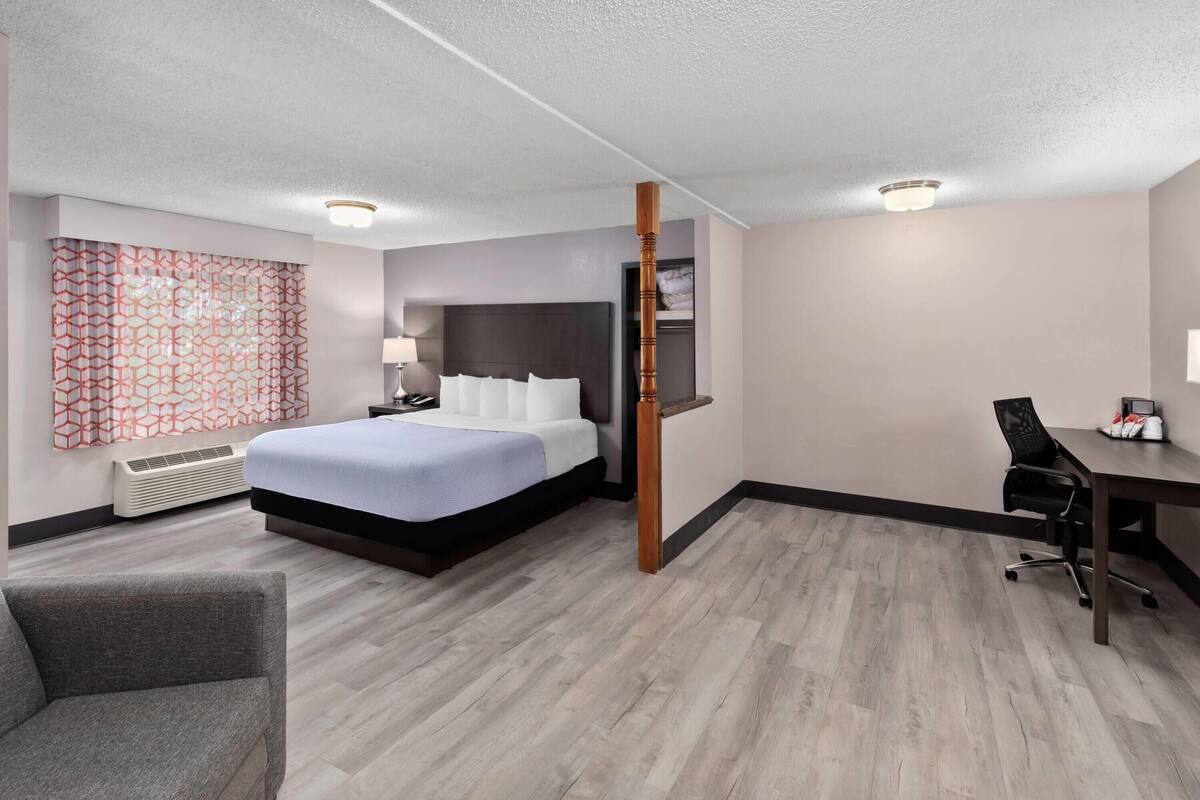 Ein Hotelzimmer mit einem großen Bett, einem Schreibtisch, einem Sessel, einer Lampe und einer dekorativen Wandverkleidung.
