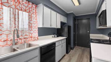 A modern kitchen with white cabinets, a stainless steel sink, and a black refrigerator.