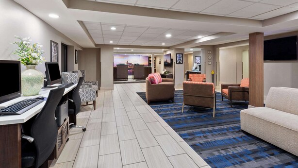 A hotel lobby with a reception desk, computers, seating area with couches, and a carpeted floor. - La Quinta Inn & Suites by Wyndham Goodlettsville - Nashville (Goodlettsville)