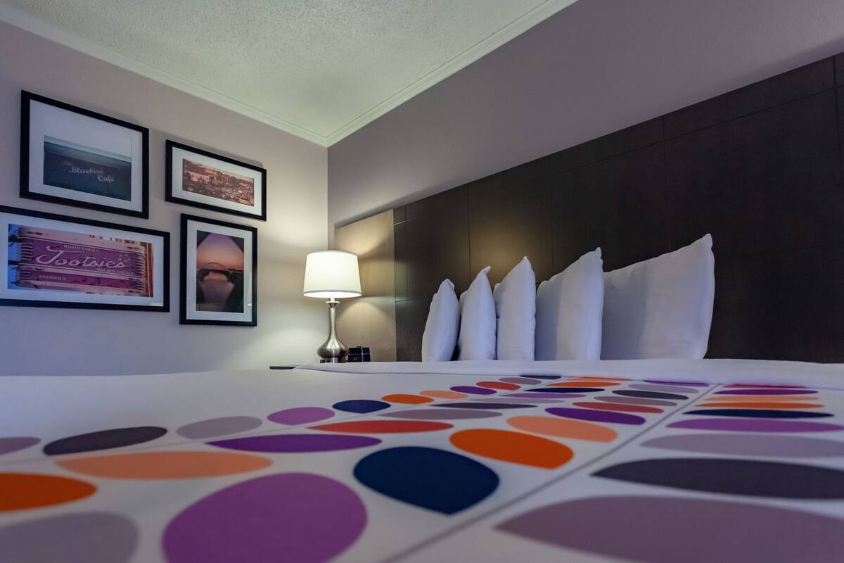 Ein Hotelzimmer mit einem Bett, einem Nachttisch, einer Lampe und gerahmten Bildern an der Wand.