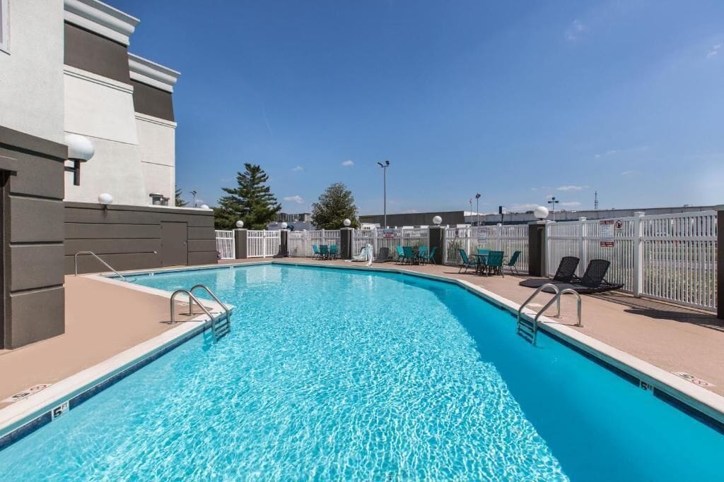 Piscina com água azul cristalina, cercada por uma grade branca e várias espreguiçadeiras.