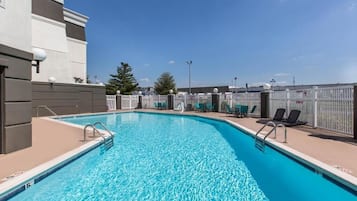 A swimming pool with clear blue water, surrounded by a white fence and several lounge chairs.