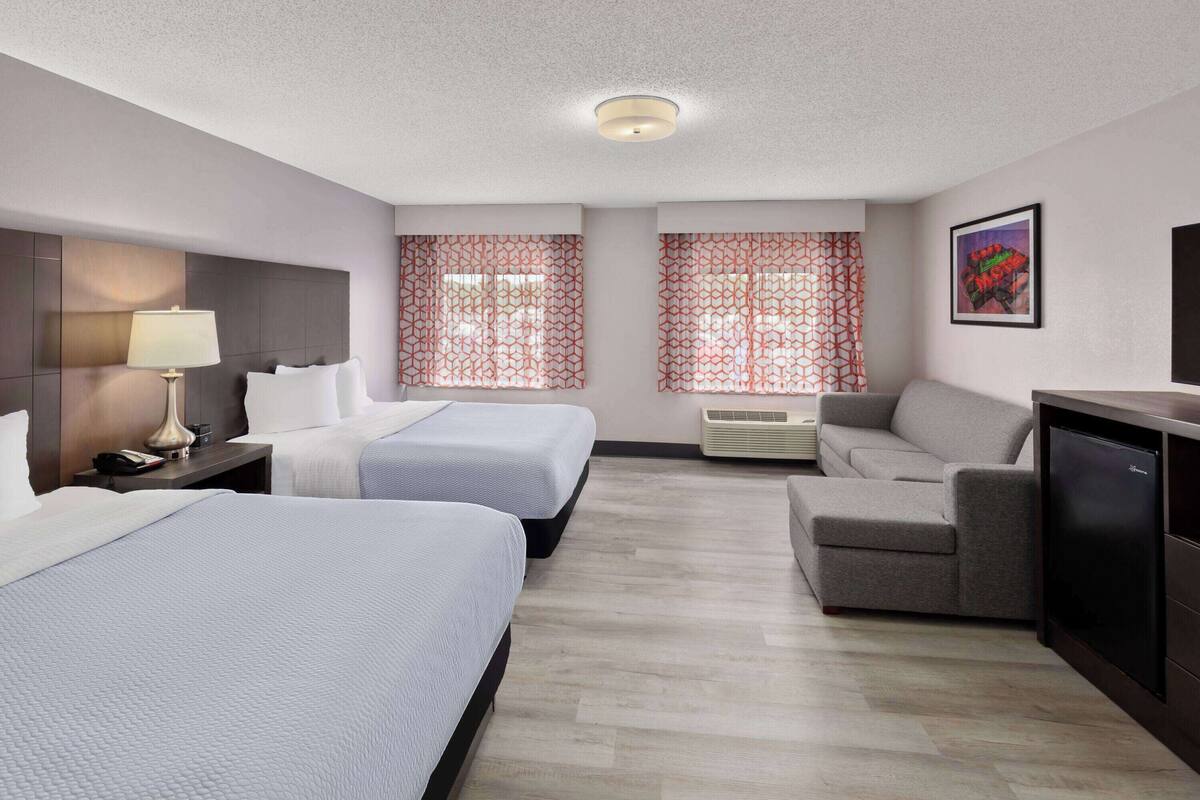 Ein Hotelzimmer mit zwei Betten, einem Schlafsofa, einem Schreibtisch und einem Fernseher.
