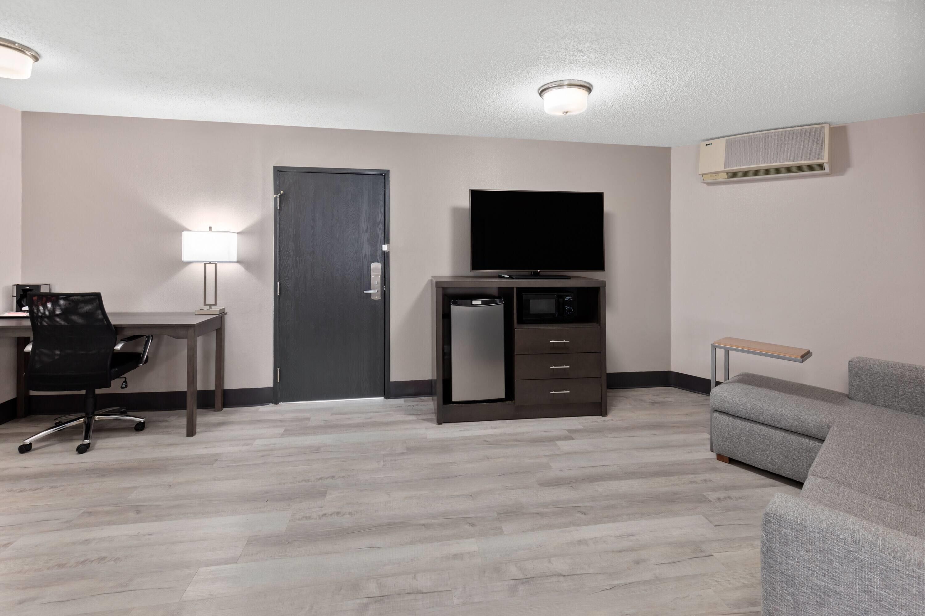 A hotel room with a desk, chair, TV, and a sofa.