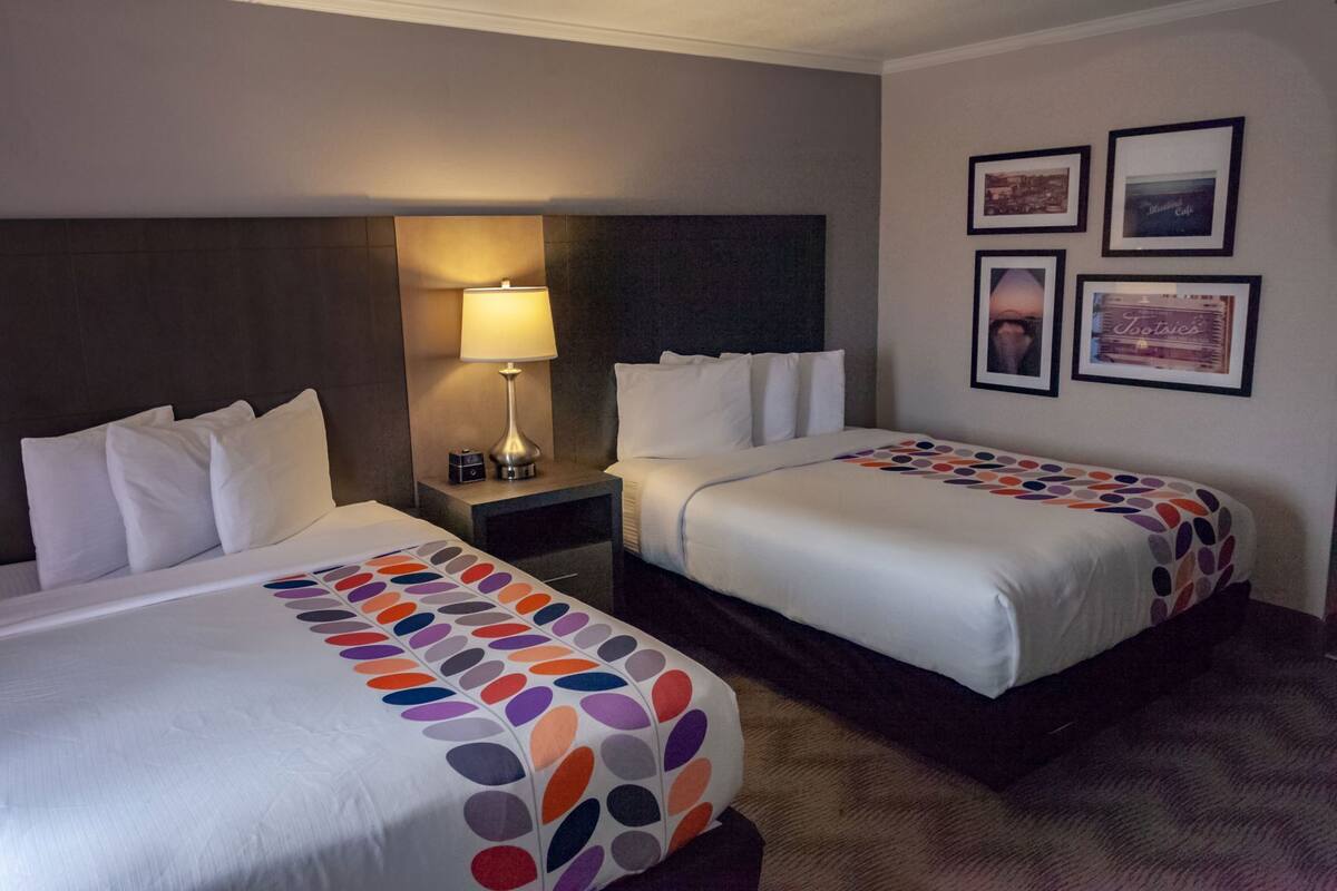 Ein Hotelzimmer mit zwei Betten, einem Nachttisch mit Lampe und gerahmten Bildern an der Wand.
