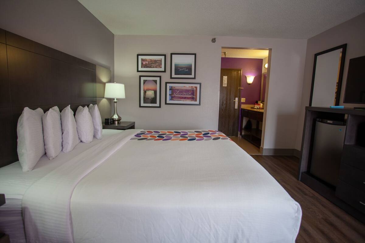 Ein Hotelzimmer mit einem großen Bett, einer Nachttischlampe, einem kleinen Tisch, einem Fernseher und einem durch eine offene Tür einsehbaren Badezimmer.