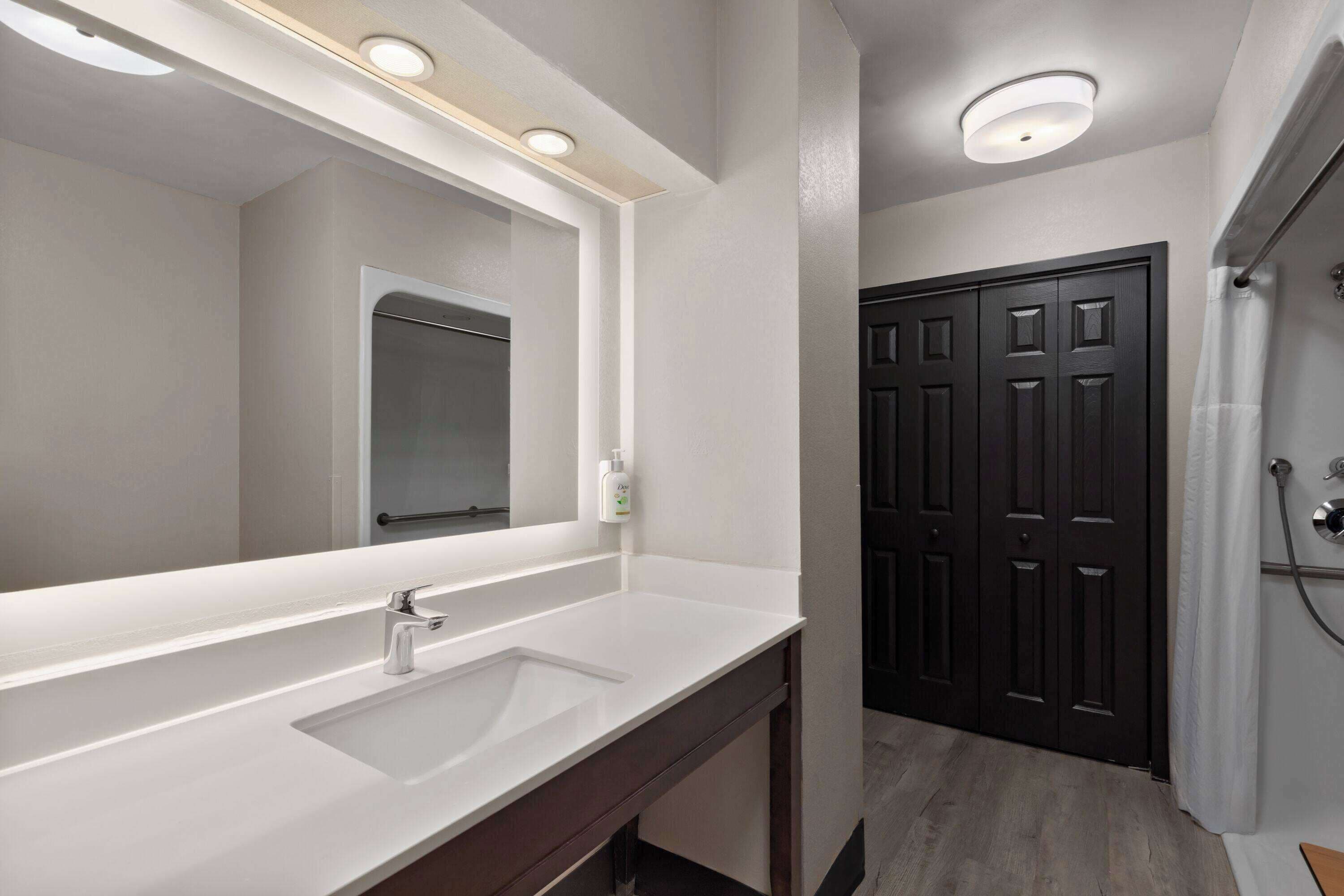 A bathroom with a white sink, a mirror, and a dark wooden door.