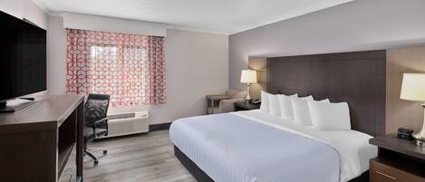Habitación de hotel con una cama grande, un escritorio, una silla, un televisor y un ventanal con cortinas estampadas.