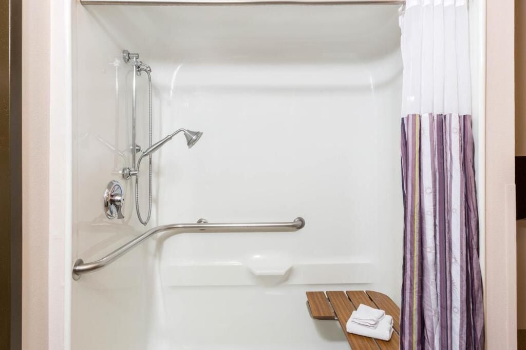 A bathroom with a shower, grab bars, a wooden bench, and a striped shower curtain.