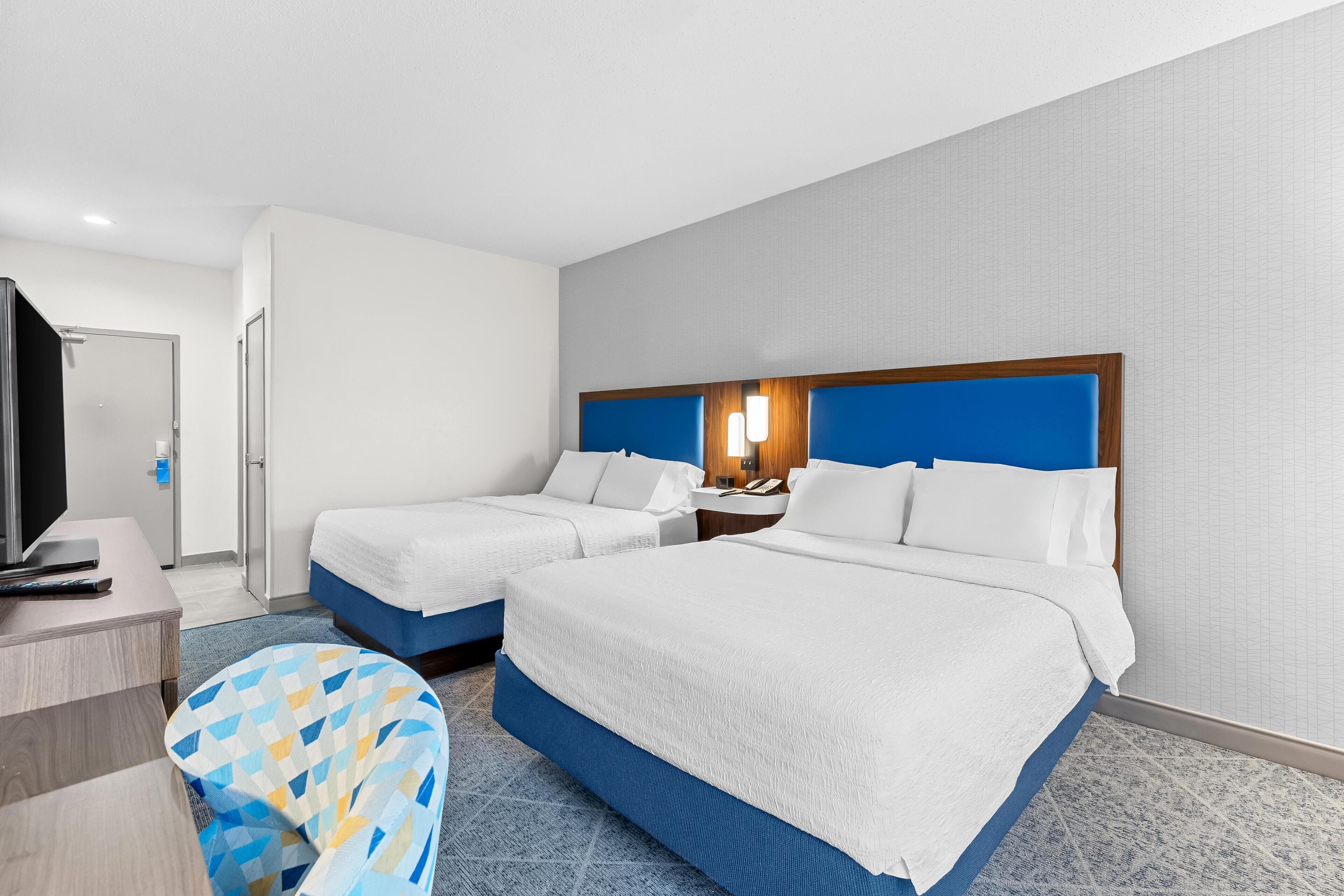 Une chambre d’hôtel avec deux lits, un bureau, une télévision et une chaise à motifs.