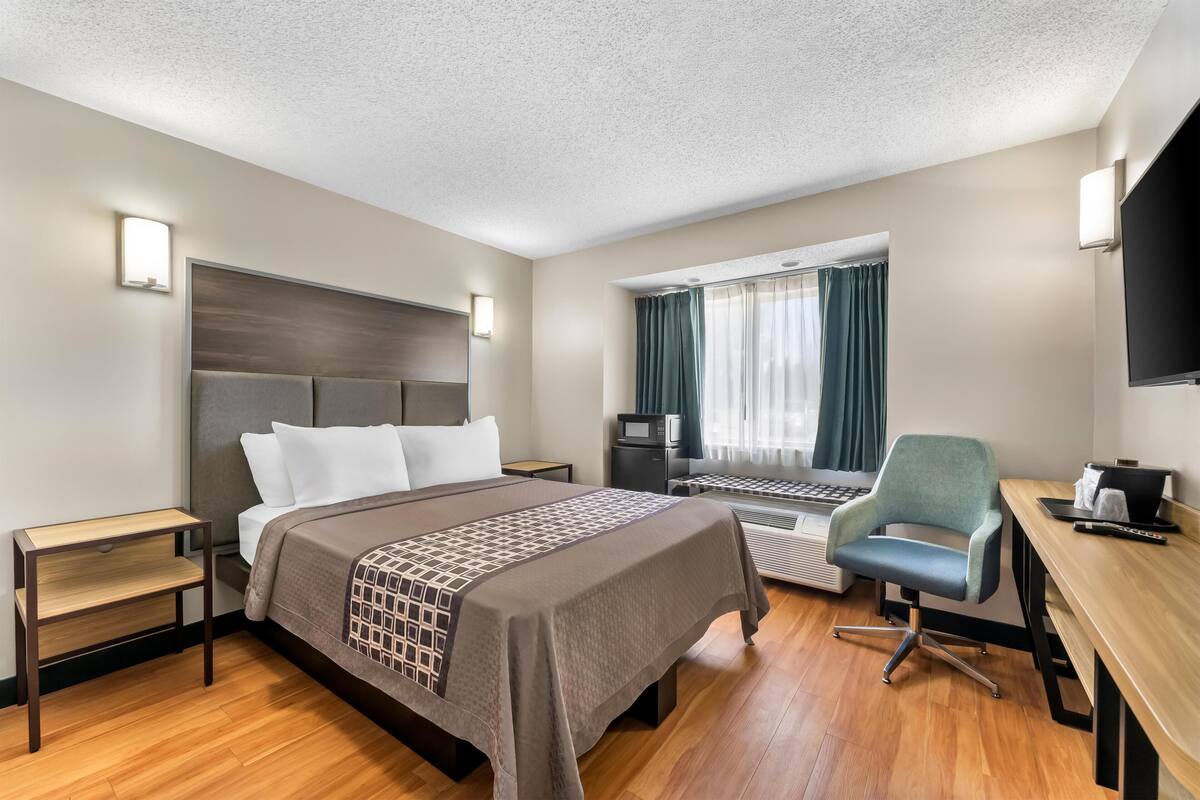 A hotel room with a bed, desk, chair, TV, and window with curtains.