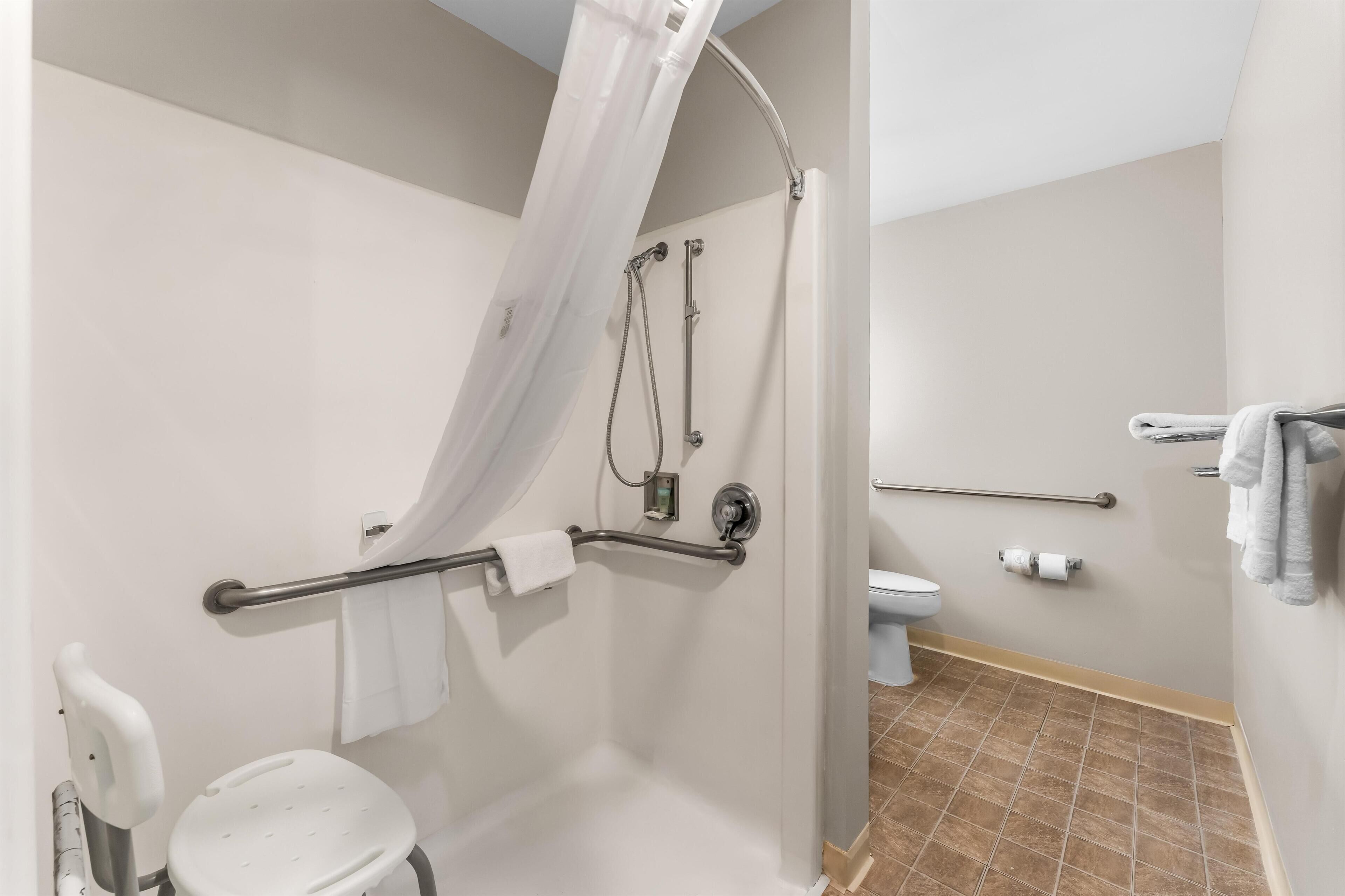Un baño con ducha, inodoro y barras de apoyo.