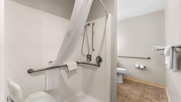 Un baño con ducha, inodoro y barras de apoyo.