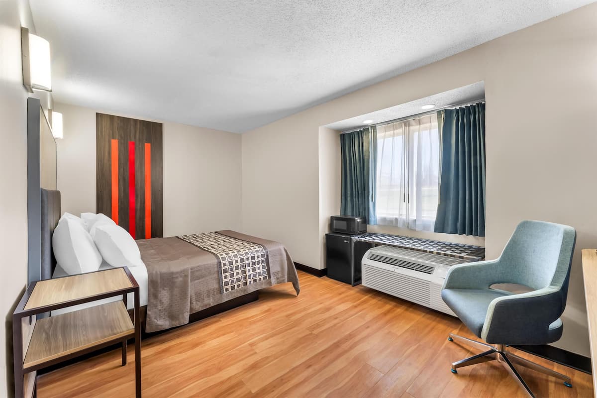 A hotel room with a bed, a desk with a computer, a chair, and a window with curtains.