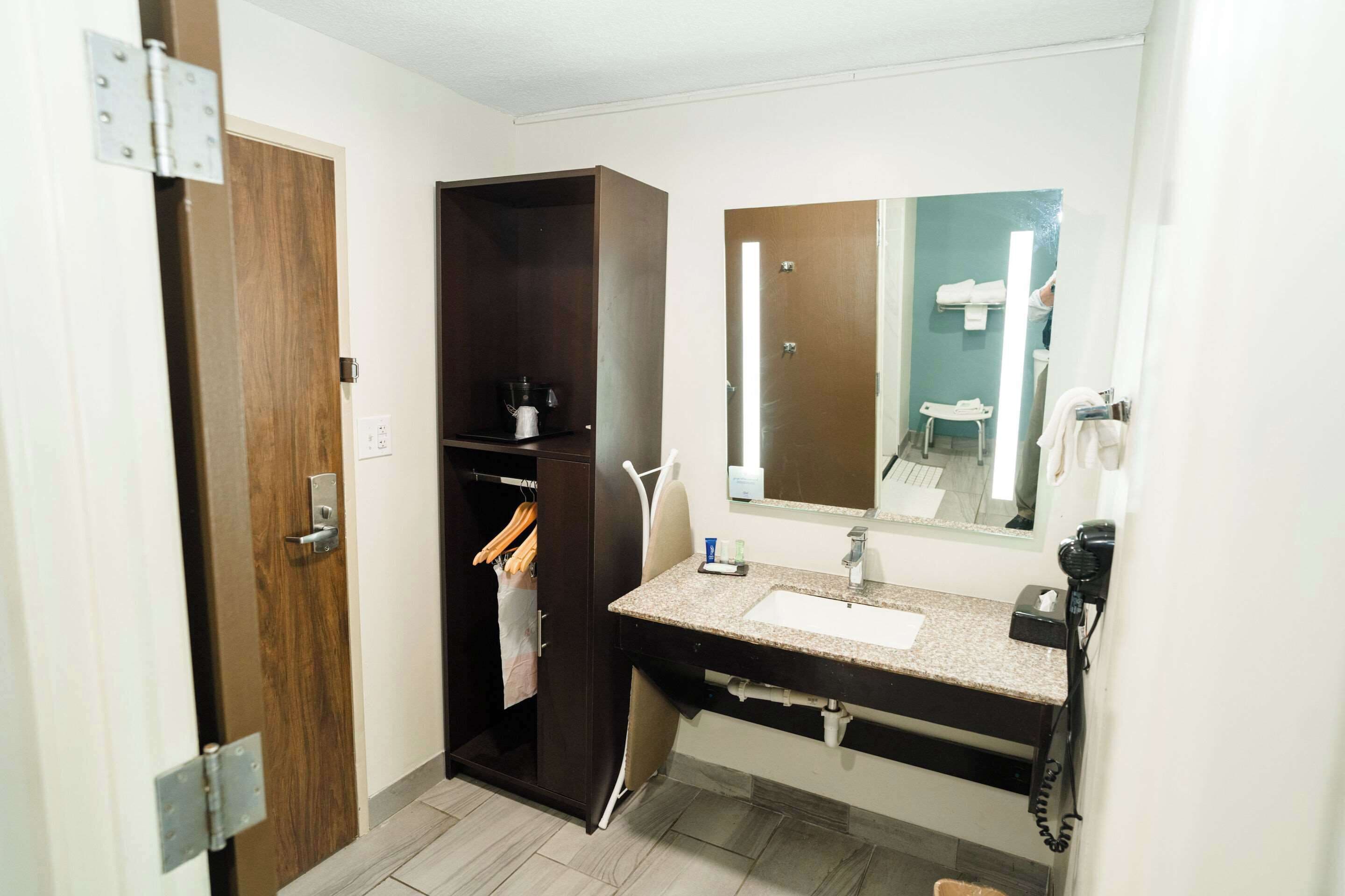 A bathroom with a wooden door, a dark wooden wardrobe, a sink with a mirror, and a hairdryer on the counter.