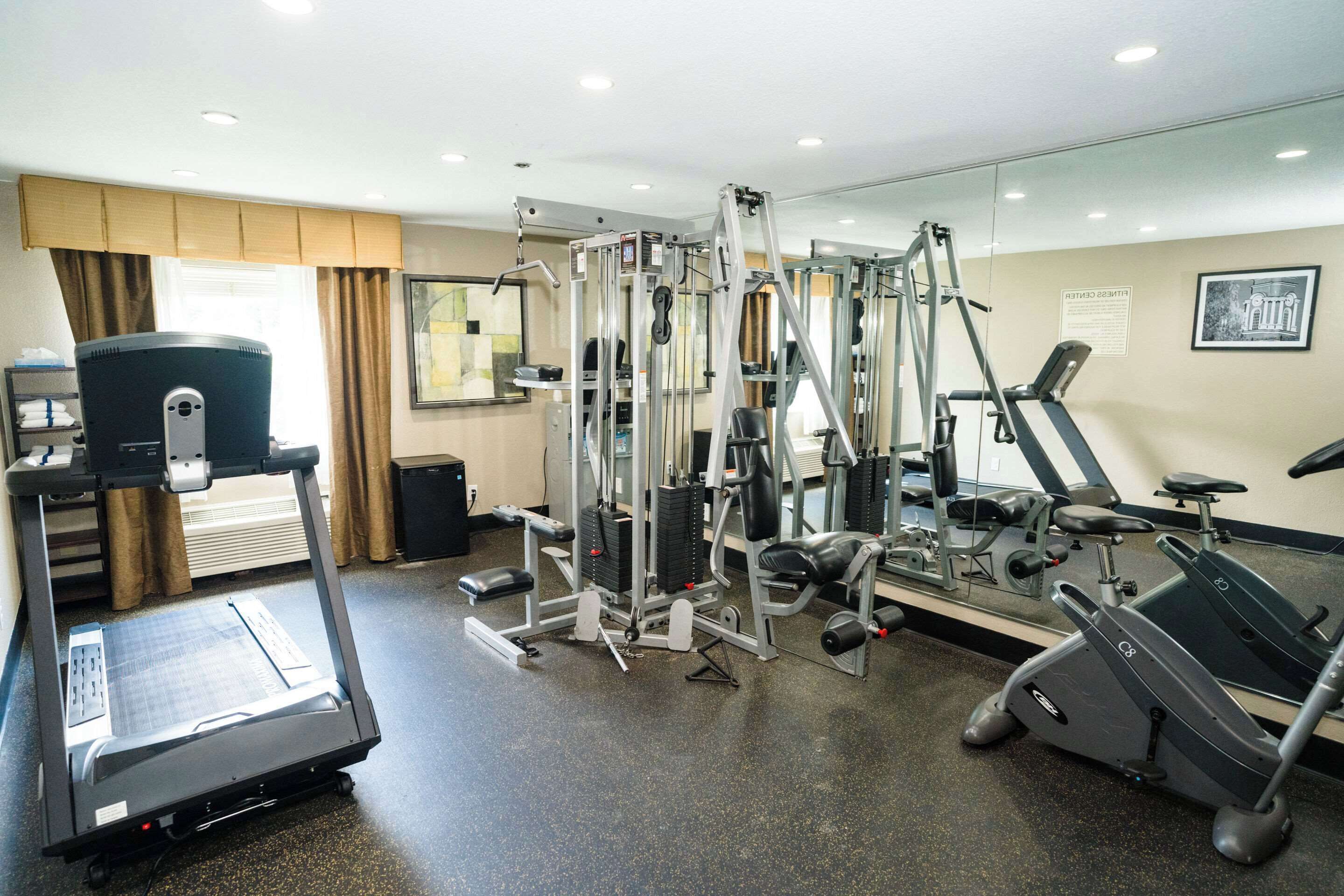 A gym with cardio machines, weight training equipment, and a mirrored wall.