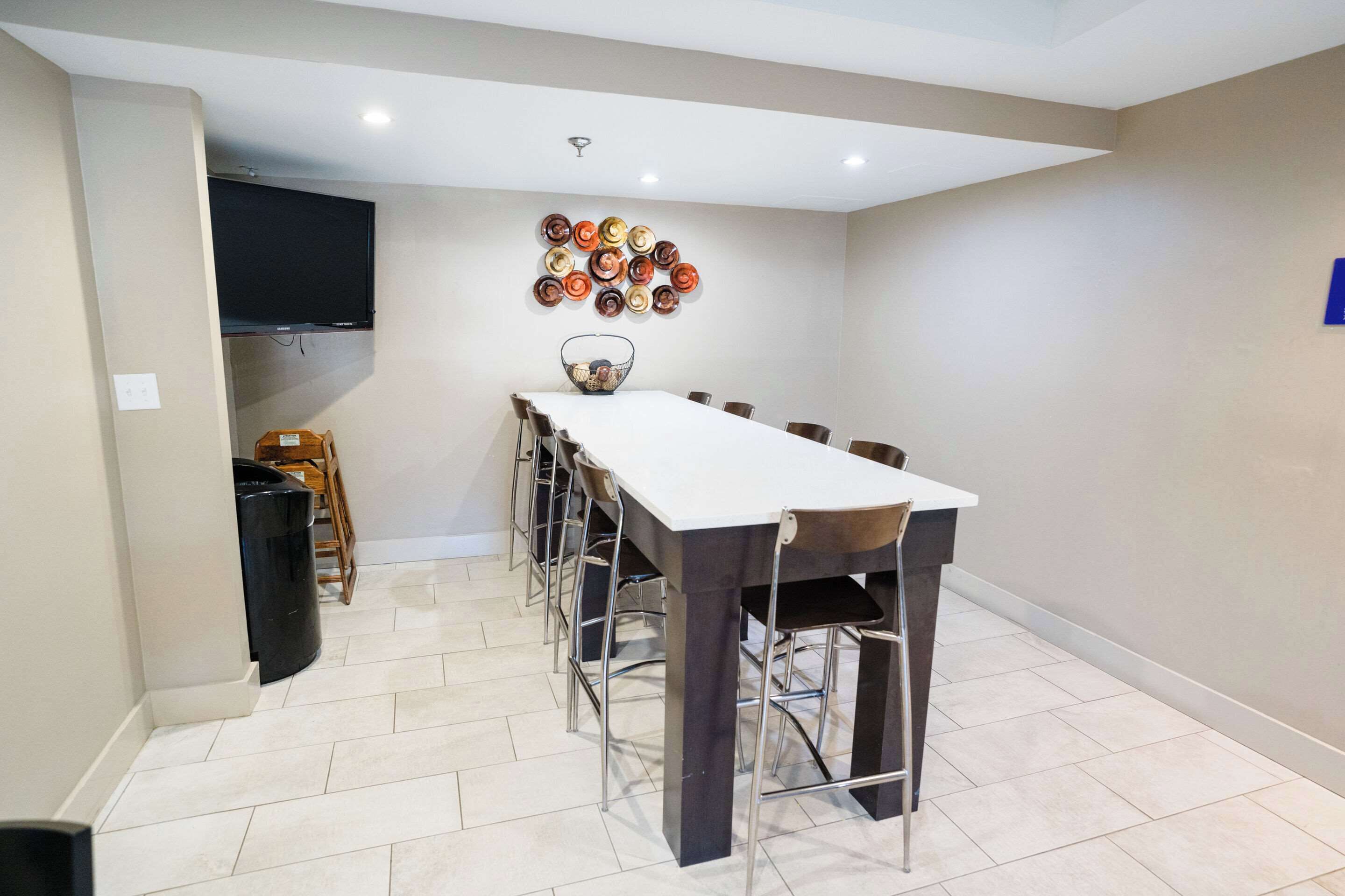 A dining area with a long table, chairs, a television mounted on the wall, and a decorative plate arrangement.
