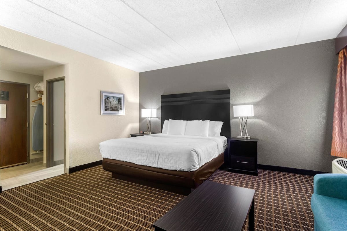 A hotel room with a bed, bedside tables, a chair, a door, and a wall-mounted picture.
