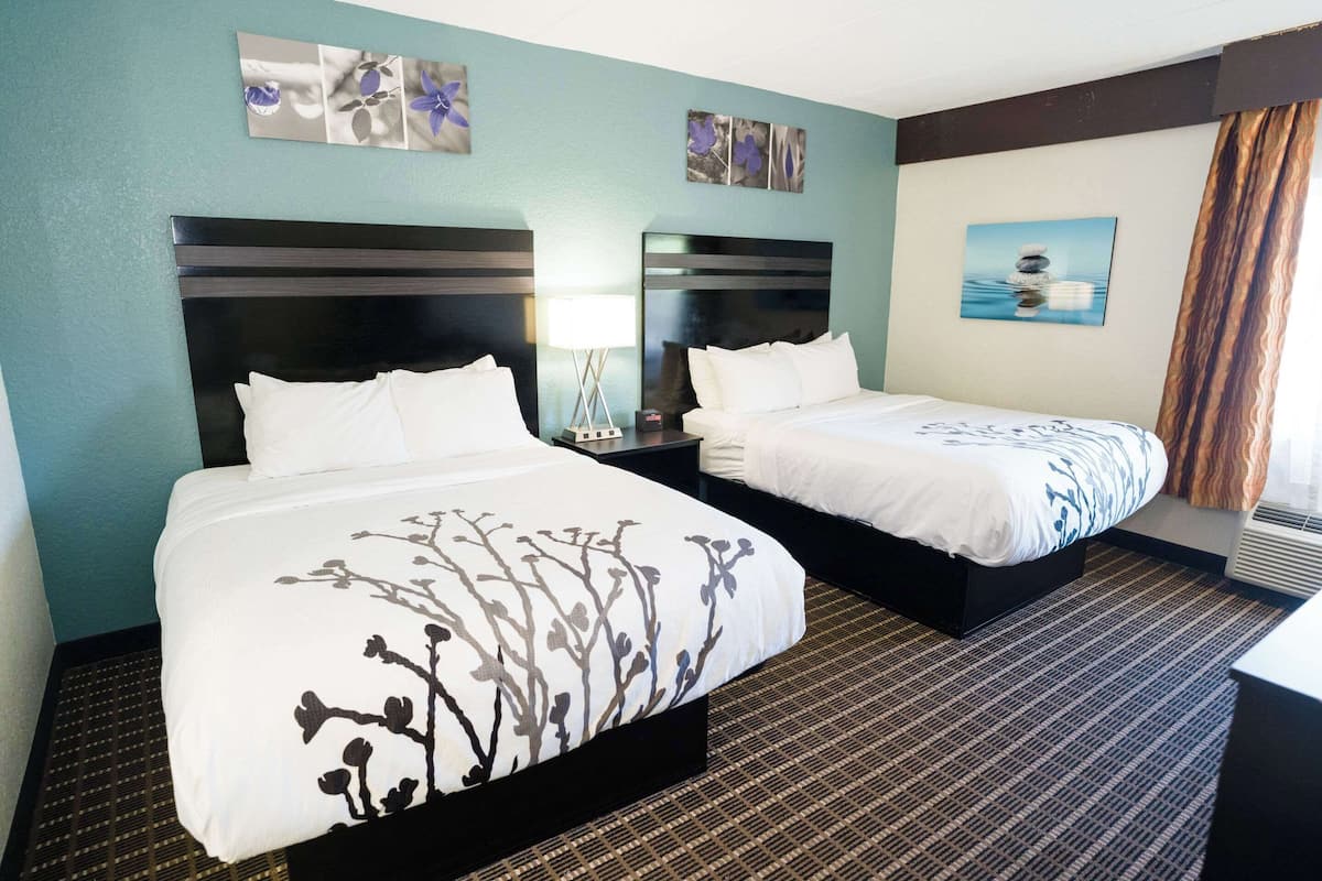 A hotel room with two beds, a large window with curtains, and artwork on the walls.