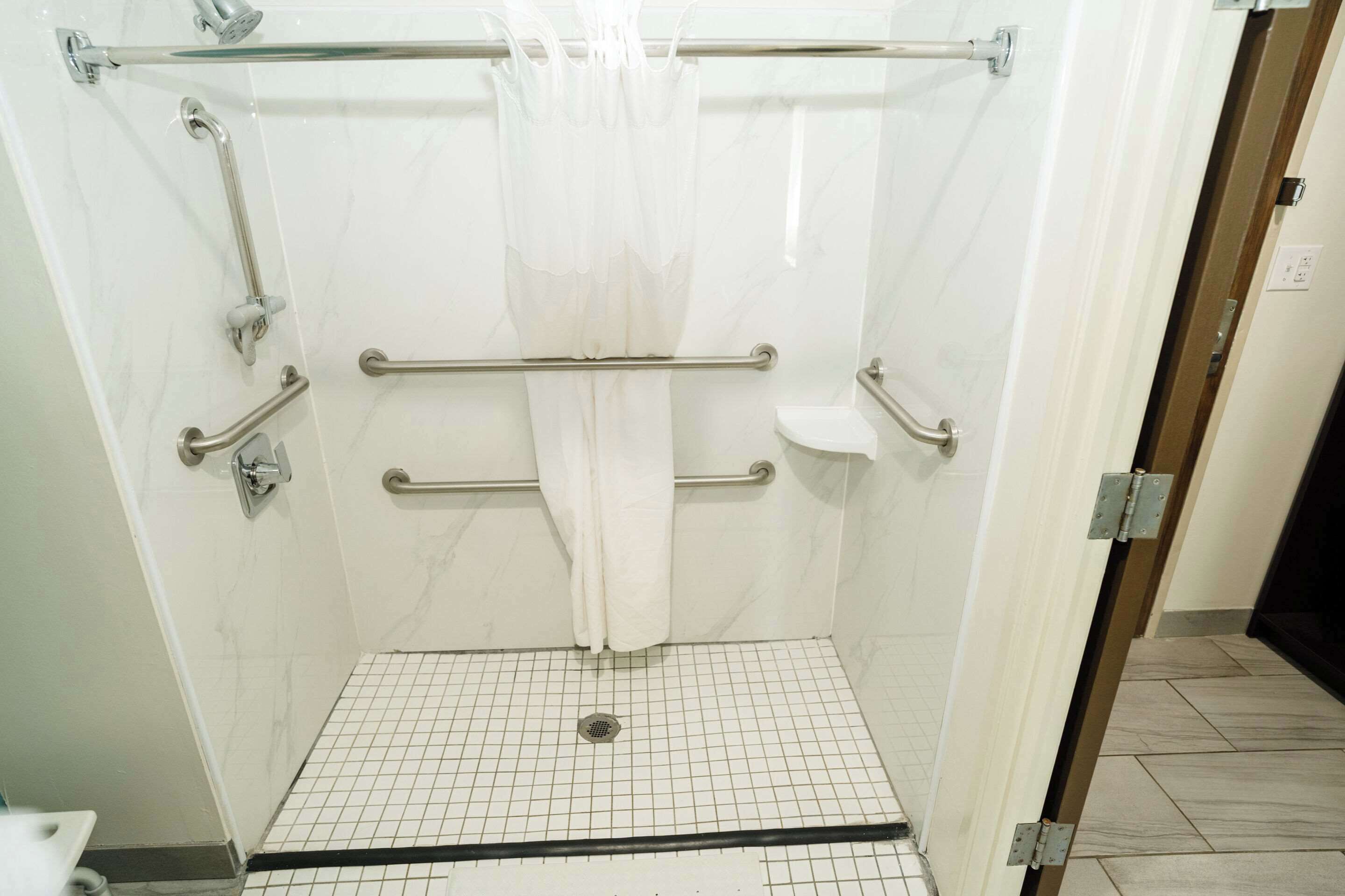 Ducha con barras de apoyo, cortina blanca y suelo de baldosas.