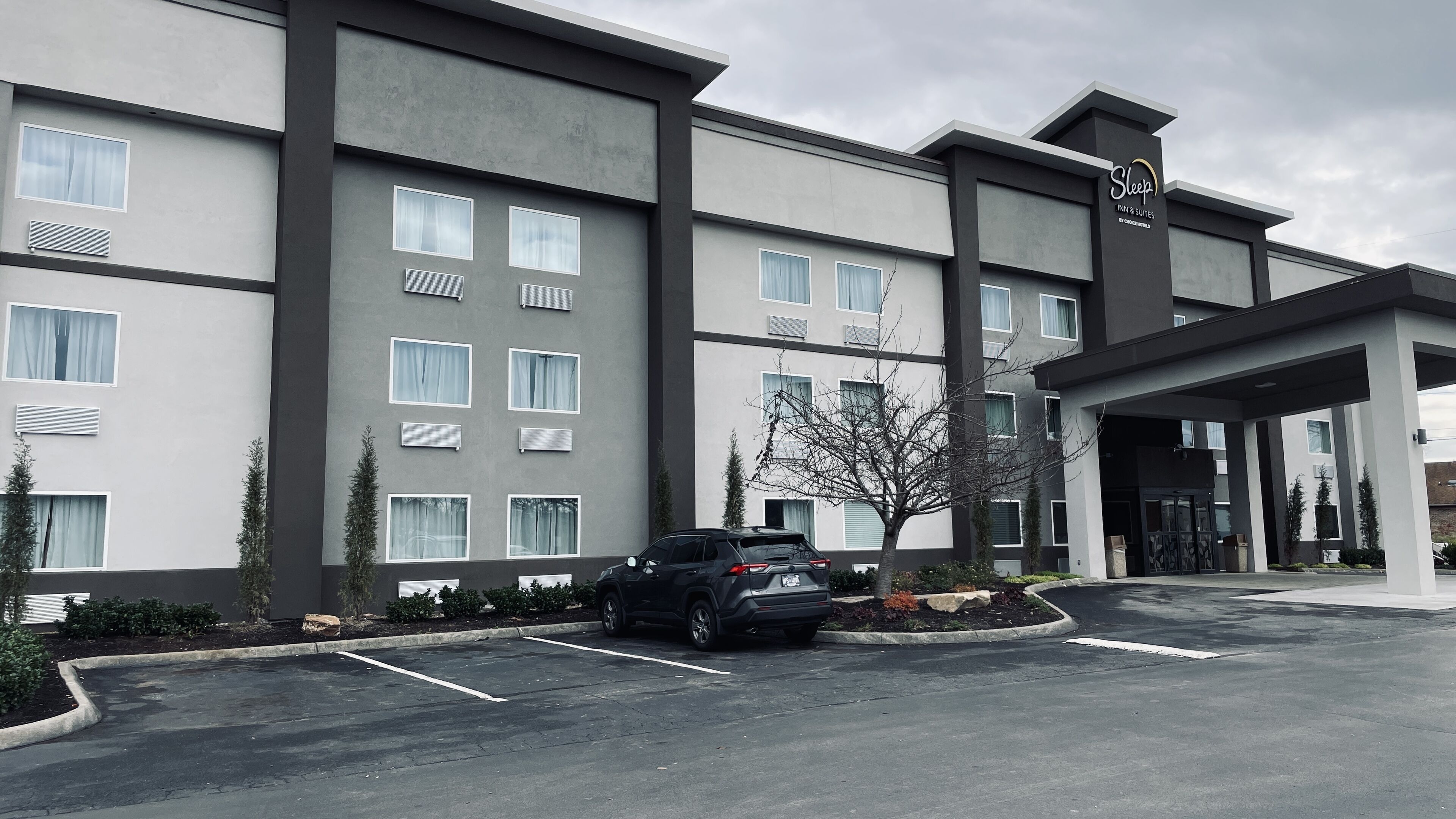 A modern hotel with a parking lot, multiple windows, and a sign for Sleep InN Suites by Choice Hotels.
