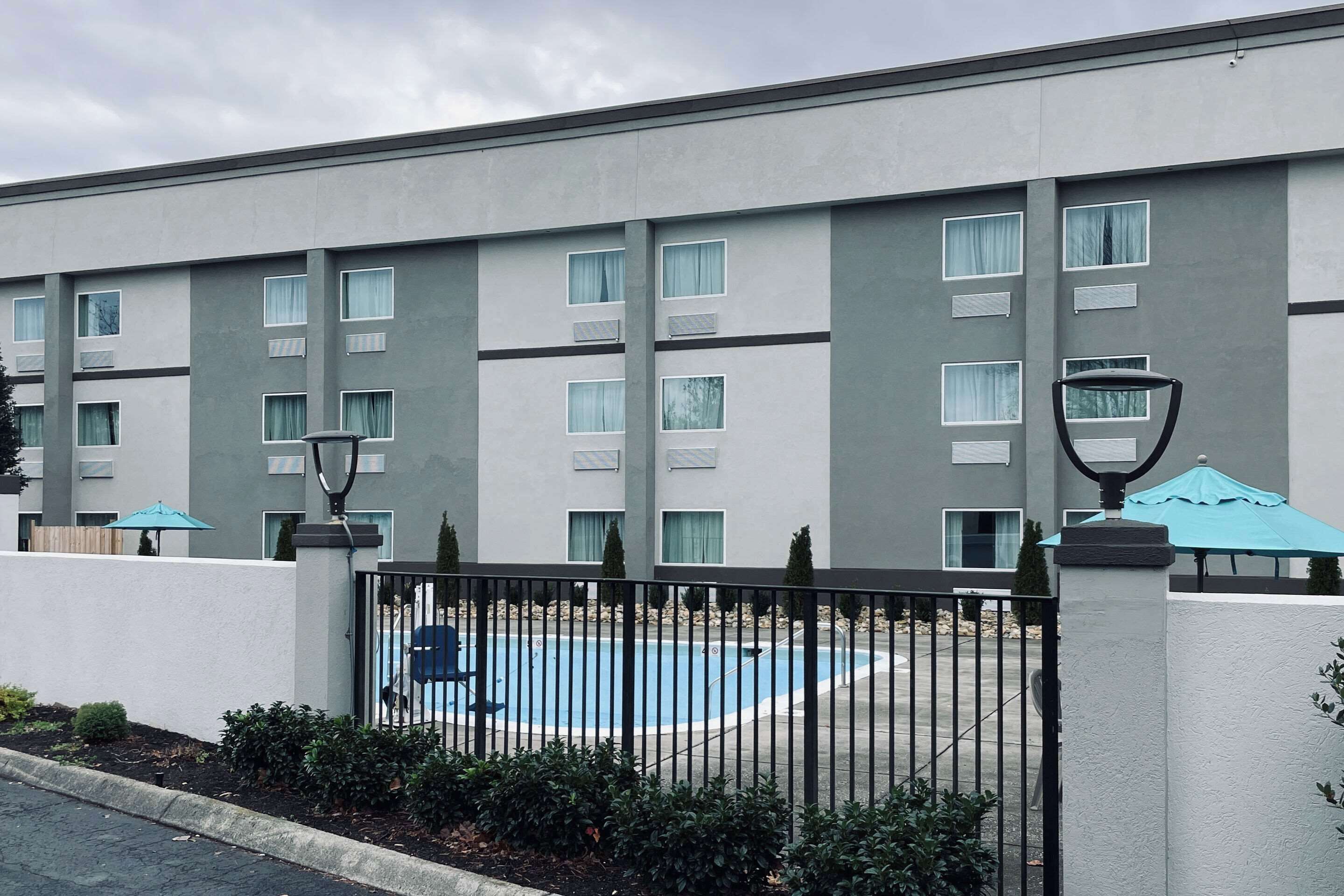 A modern hotel with a swimming pool, a gated entrance, and a landscaped area with bushes.
