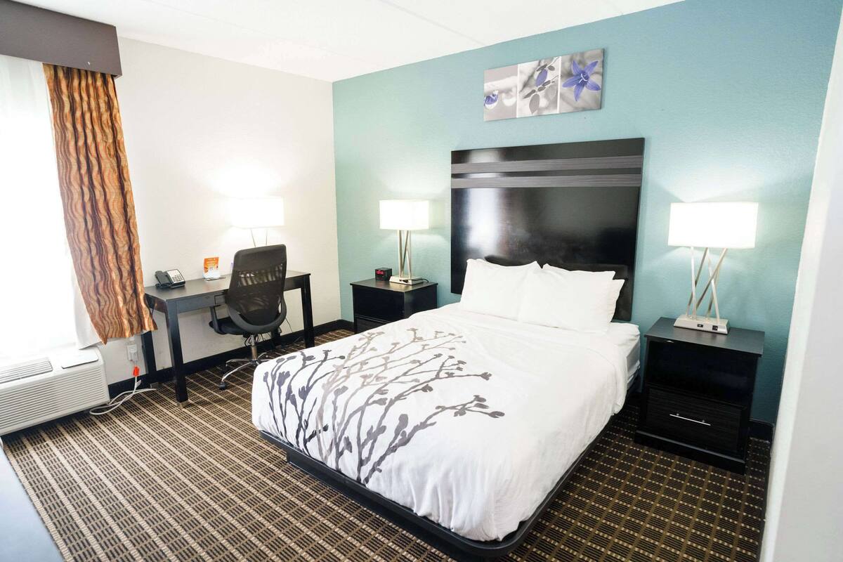 A hotel room with a large bed, two bedside tables with lamps, a desk with a chair, and a wall-mounted artwork.