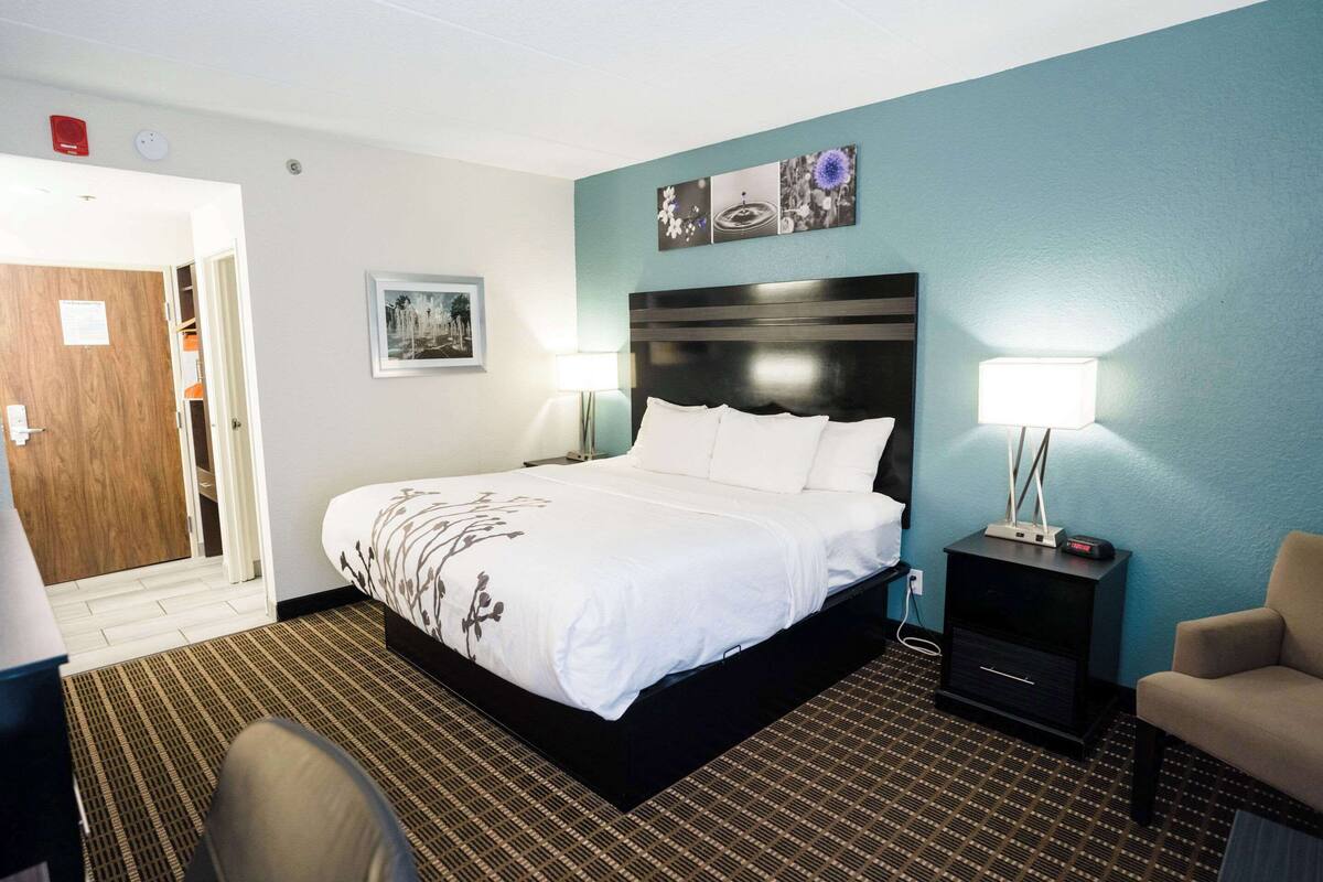 A hotel room with a large bed, two bedside tables, a chair, and a door leading to the hallway.