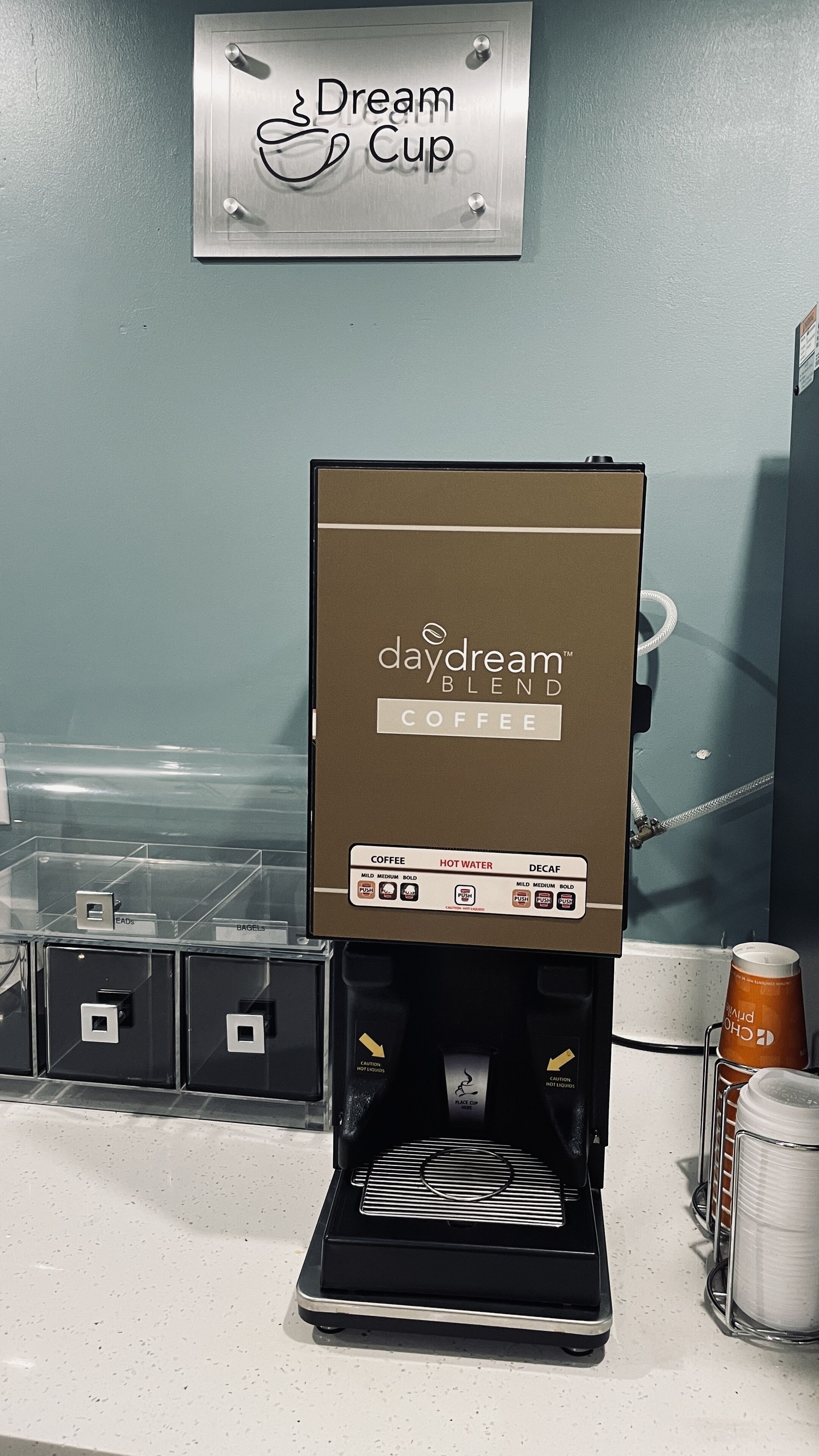 En kaffemaskine med en brun kasse med påskriften "daydream blend coffee" og valgmuligheder for kaffe, varmt vand og koffeinfri kaffe.