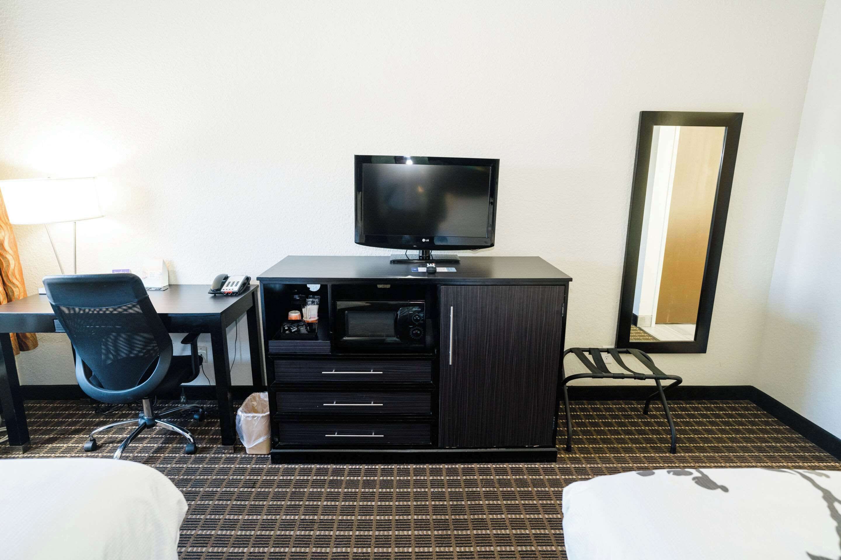 A hotel room with a bed, a desk with a computer, a television, a chair, and a wardrobe.