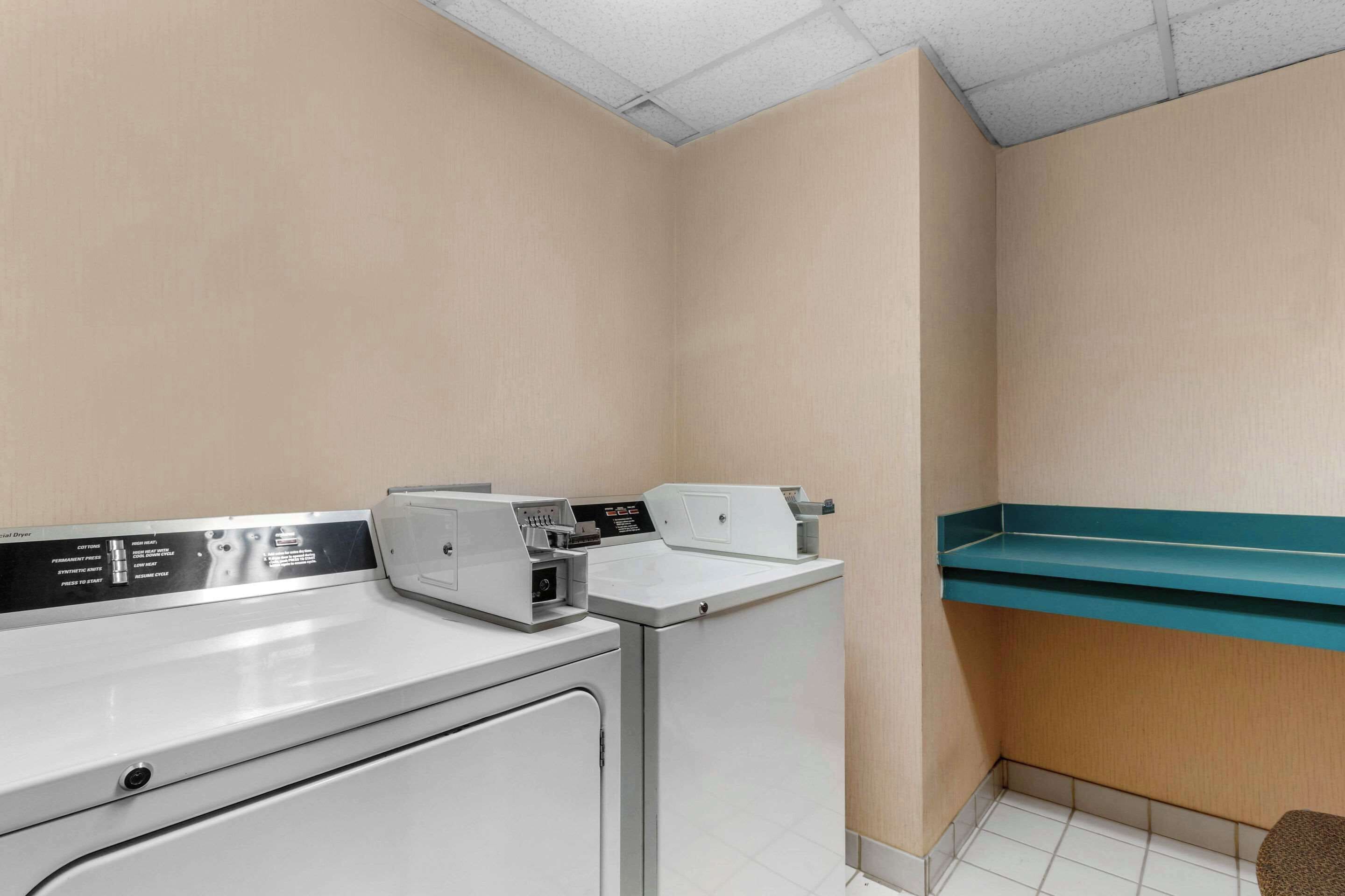 A laundry room with two washing machines, a drying rack, and a control panel.