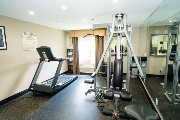 Un gimnasio con cinta de correr, máquinas de pesas y un espejo.