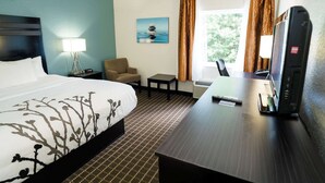 Een hotelkamer met een groot bed, een bureau met een computer, een stoel, een klein tafeltje en een raam met gordijnen.