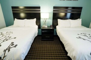A hotel room with two beds, a nightstand with a lamp, and a small table.