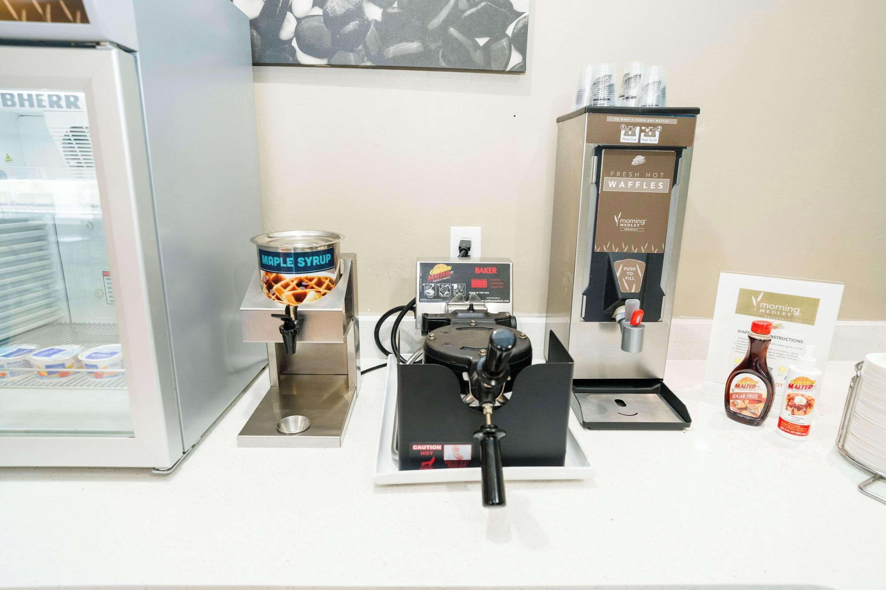 A coffee station with a syrup dispenser, a waffle maker, and a fresh hot waffle dispenser.